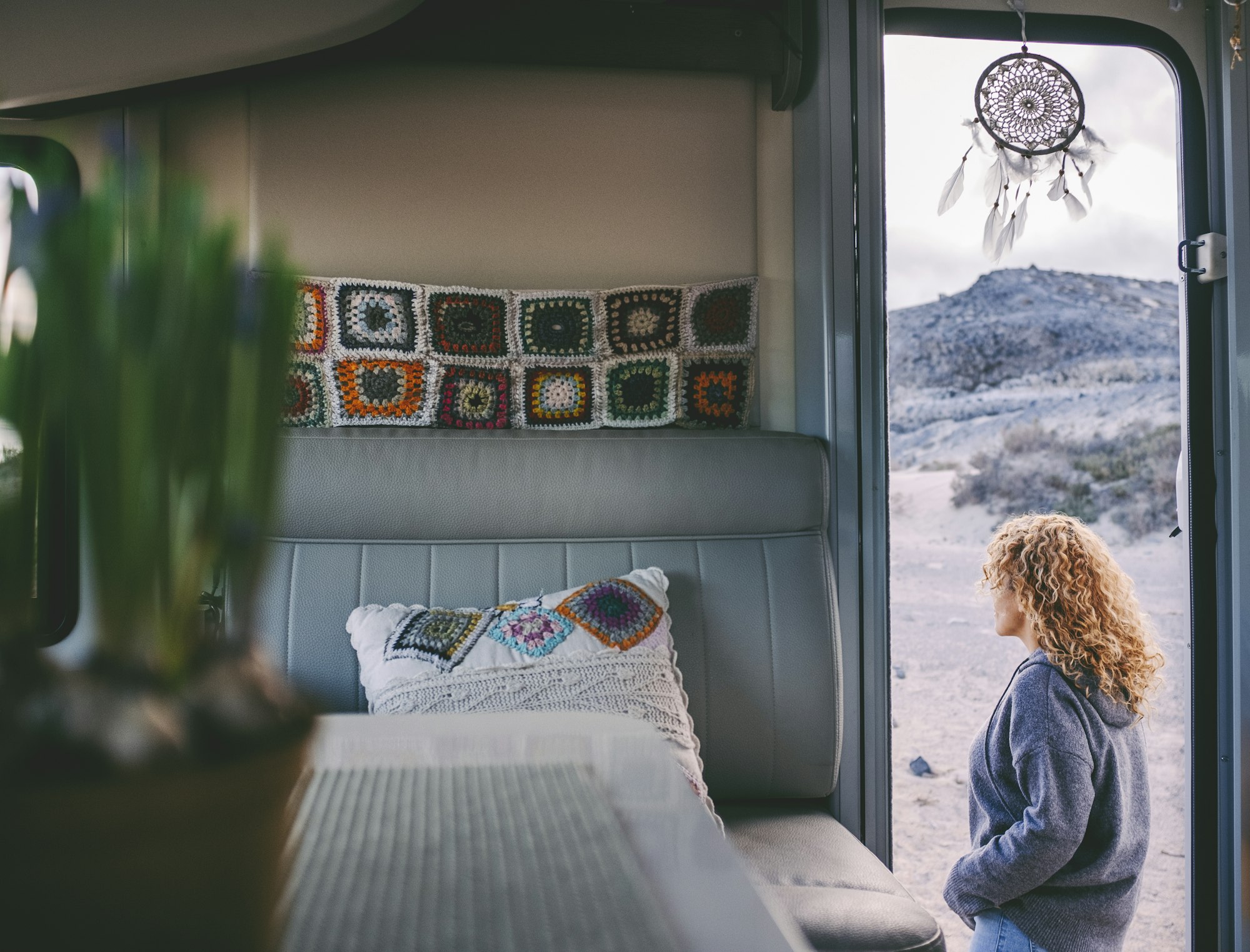 Woman walking outside her camper van. View from interior. Knit decorations inside.